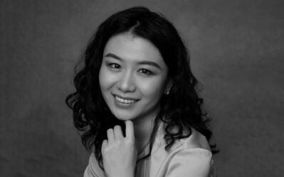 A person with curly hair smiling and resting their chin on their hand in a black and white portrait.