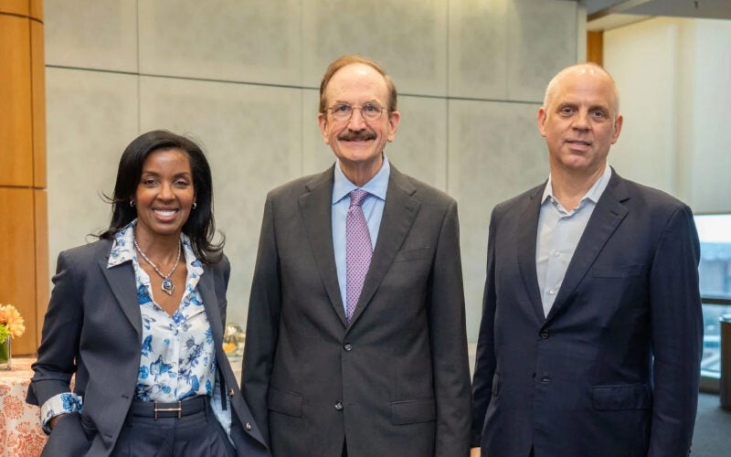 A small group of three professionally dressed individuals standing together indoors, smiling at the camera.